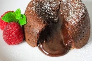 cut open chocolate lava cake with powdered sugar on top and raspberries and mint beside it.