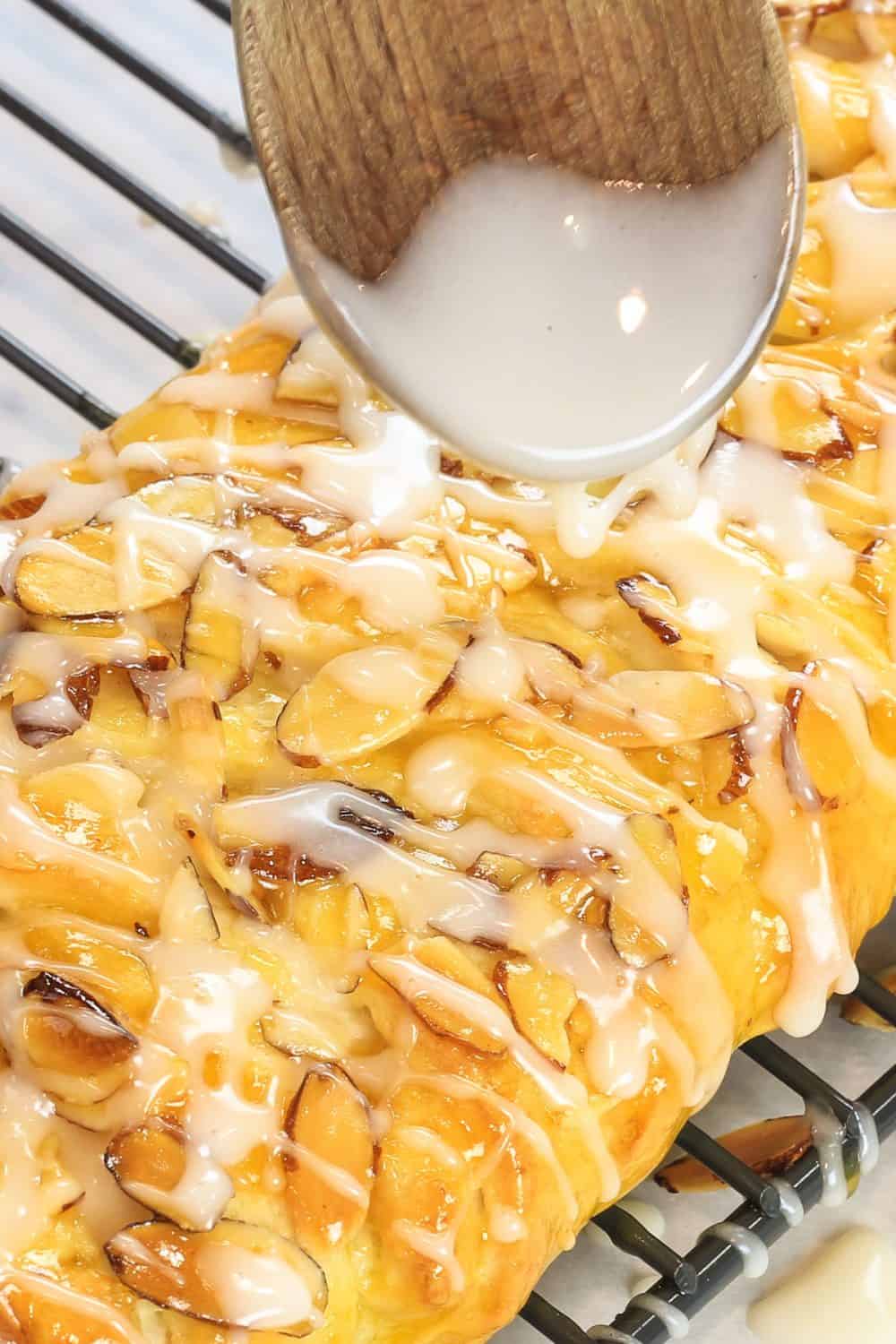 Overhead picture of icing being drizzled over the top of the prepared danish recipe that has been topped with sliced almonds