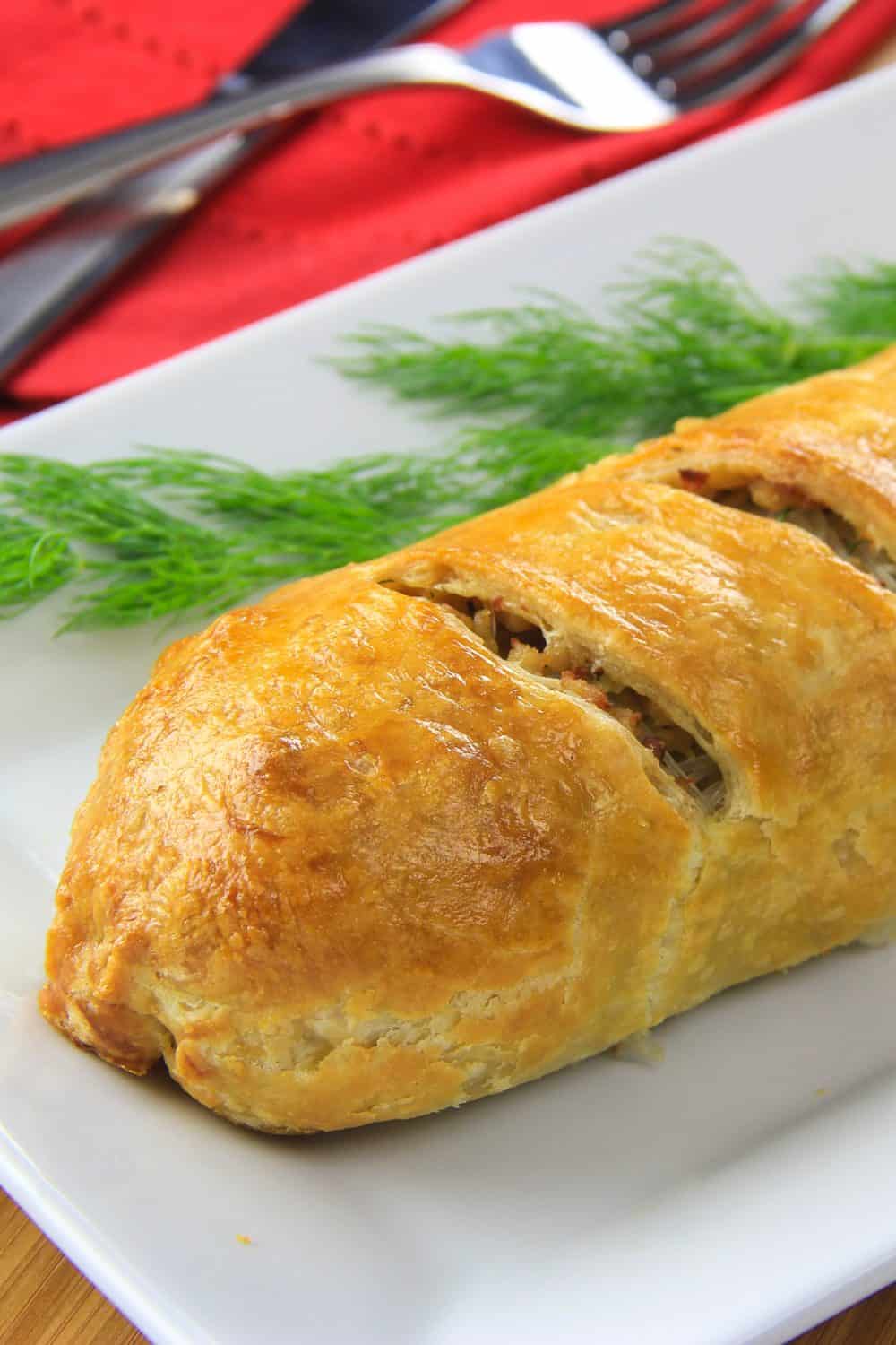 Prepared chicken puff pastry served on a white plate with fresh dill and a red napkin with fork and knife