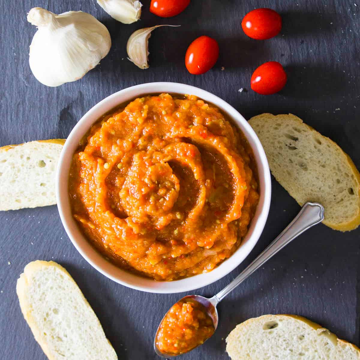 eggplant spread ikra, in a white bowl with tomatoes and bread around