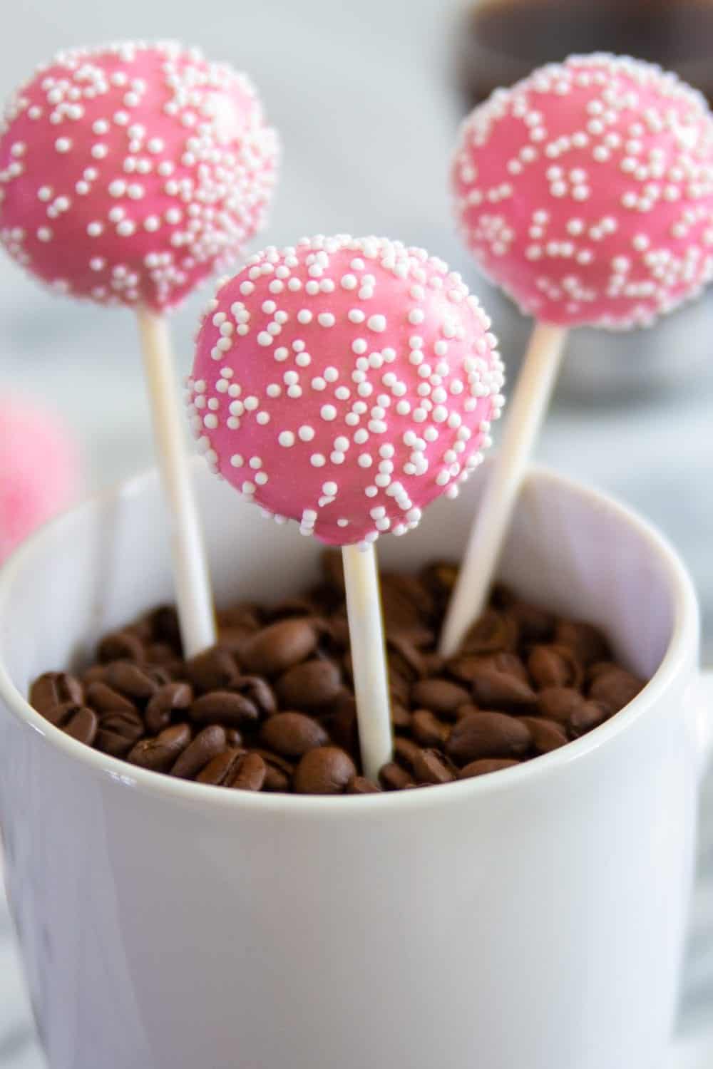 pink cake pops in a white mug filled with coffee beans 