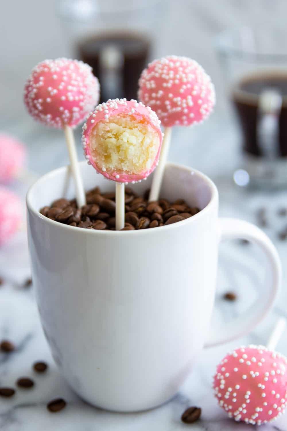 pink cake pops in a white mug filled with coffee beans