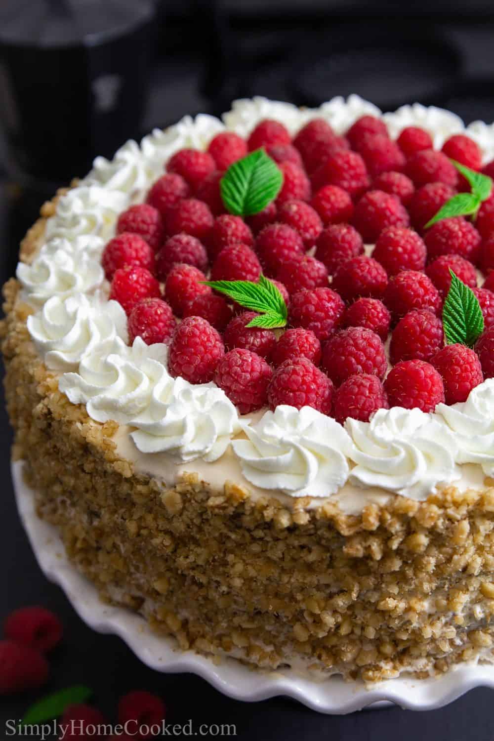 Honey raspberry cake sitting on a white cake stand on a black surface with a dark background