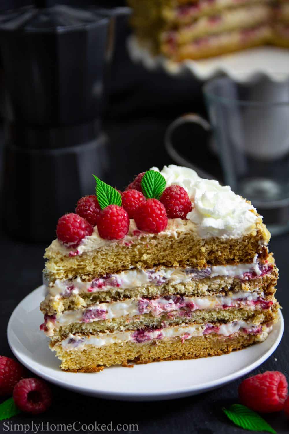 A slice of honey raspberry cake sitting on a white plate that is sitting on a black table and background