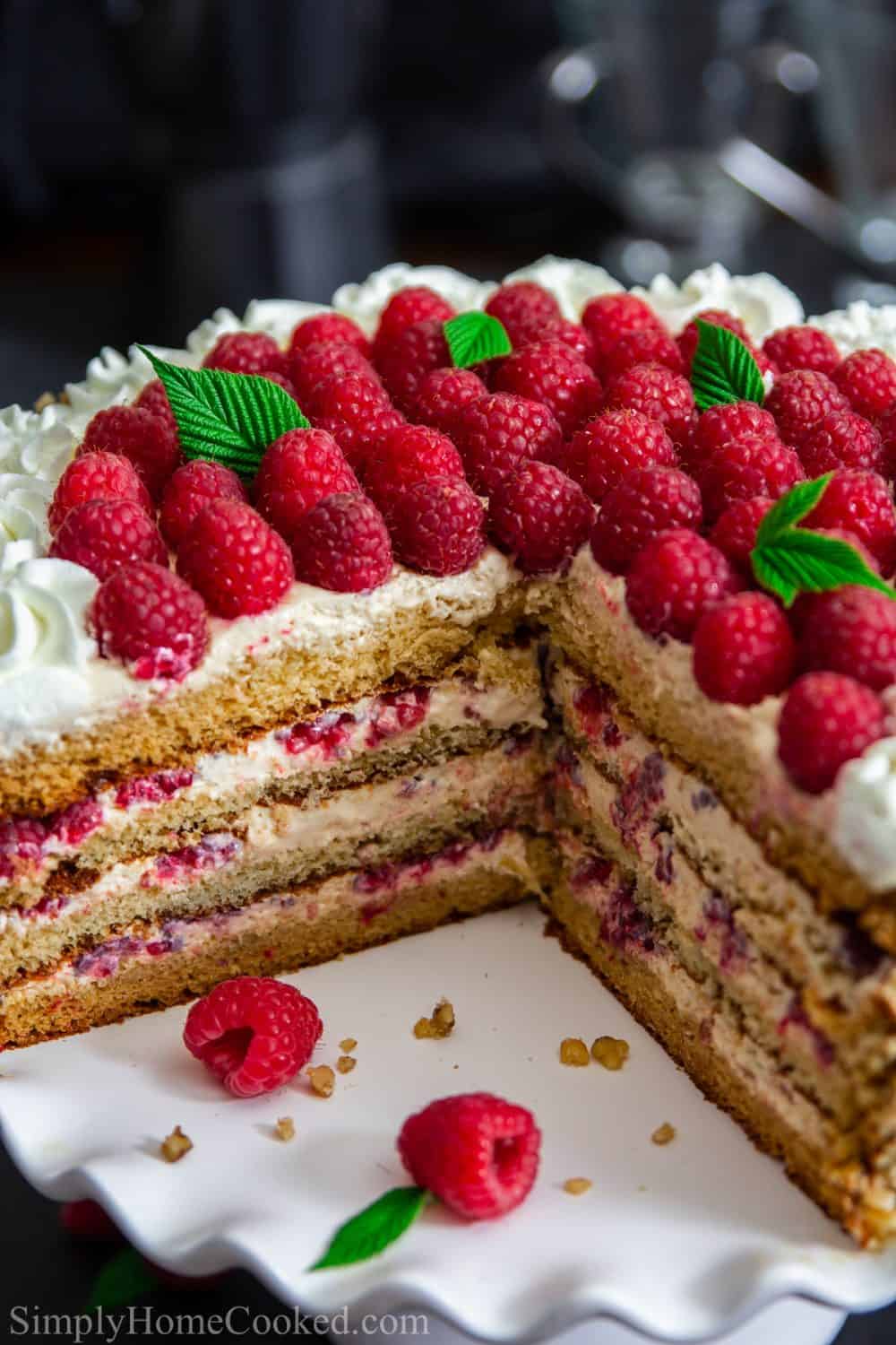 Up close photograph of the honey raspberry cake with a slice cut out and the interior layers showing while sitting on a white cake stand with a dark background