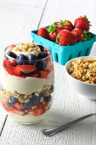 greek yogurt berry parfait with a bowl of granola and basket of strawberries beside it