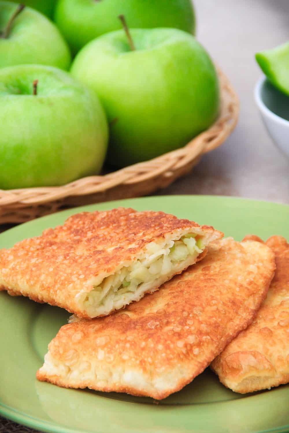 close up image of homemade fried apple turnovers on a green plate with granny smith apples in the background