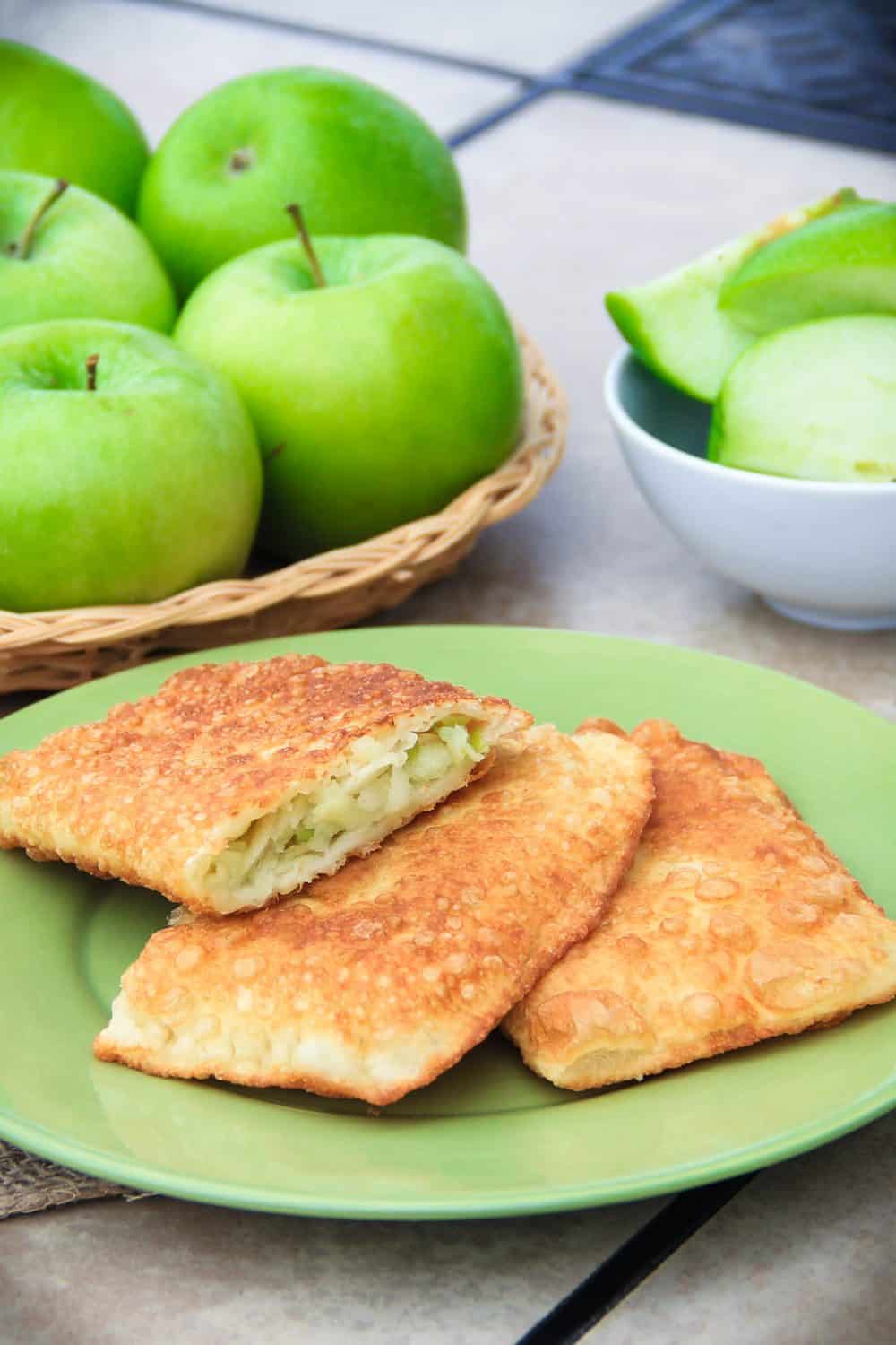 from scratch made apple turnovers on a green plate with sliced granny smith apple wedges in the background 