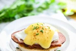 eggs Benedict on a white plate with parsley behind it