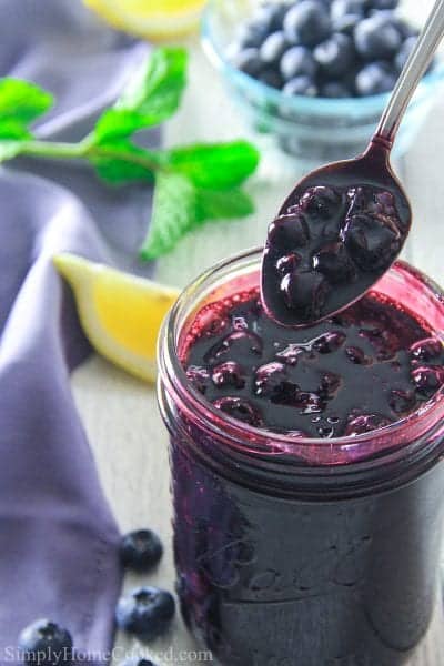 blueberry pie filling in a mason jar with a spoon and lemons around it