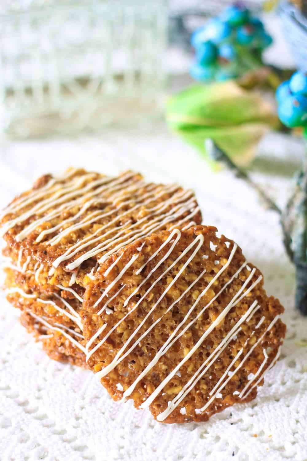 Photograph of a stack of florentine cookies with white chocolate drizzle laying on a lace tablecloth