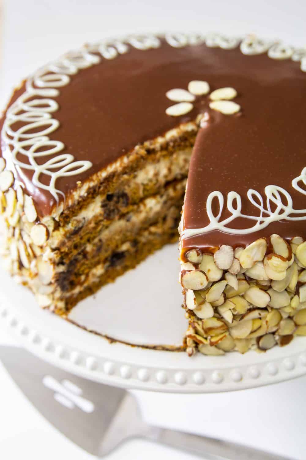 Poppy Seed Honey Cake covered in chocolate ganache and sliced almonds, with one slice cut out on a white plate and white background.