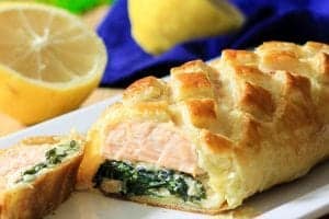 Sliced salmon Wellington in a white dish with sliced lemon around it