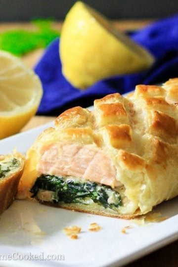 Sliced salmon Wellington in a white dish with sliced lemon around it