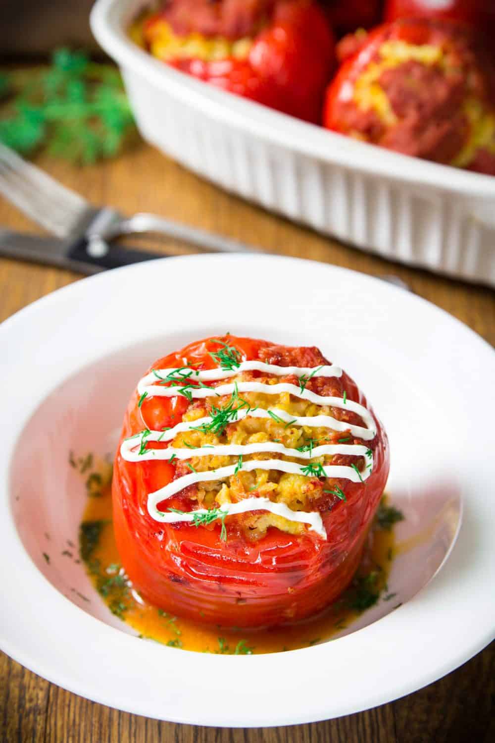 slavic russian rice and chicken stuffed red peppers served on a white plate with sour cream and dill on top