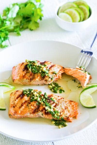 grilled cilantro lime salmon on a white plate with sliced lime beside it.