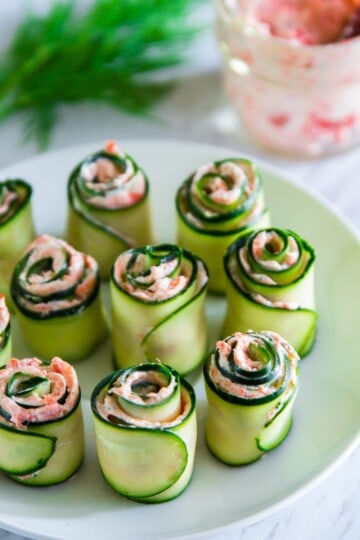 smoked salmon spread rolled inside of thinly sliced cucumbers on a white plate