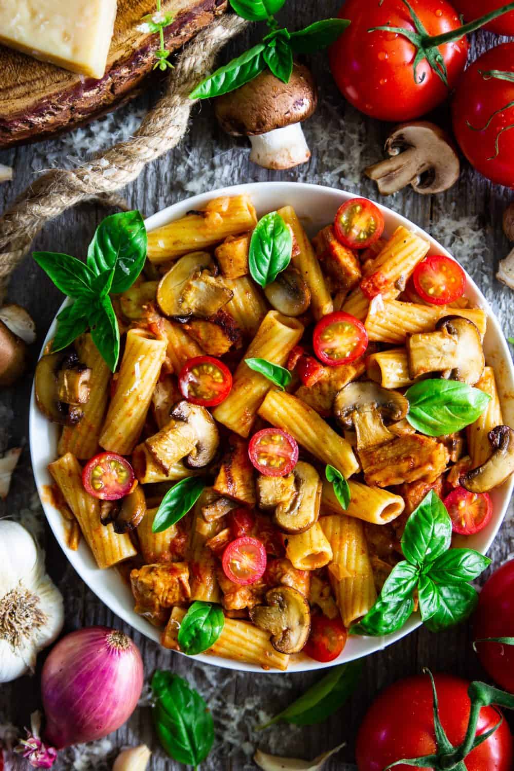 Delicious Mushroom Pasta Recipe with grilled chicken, cajun spices, basil and cherry tomatoes displayed with fresh vegetables in large bowl. 