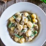 creamy mushroom gnocchi with spinach in a white bowl with fresh spinach and raw mushrooms beside it