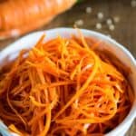 shredded carrot salad in a white bowl with coriander sprinkled next to it