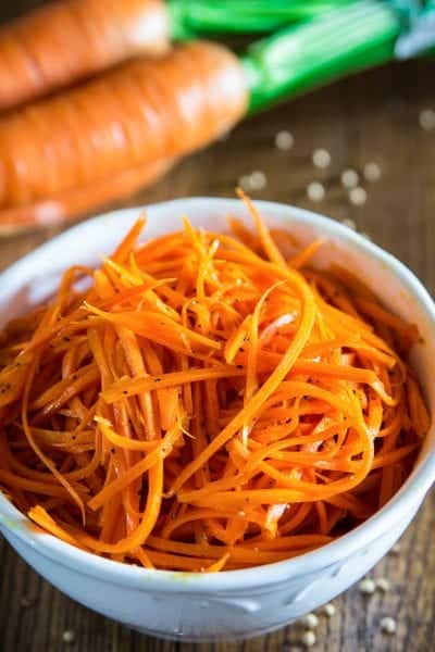 shredded carrot salad in a white bowl with coriander sprinkled next to it