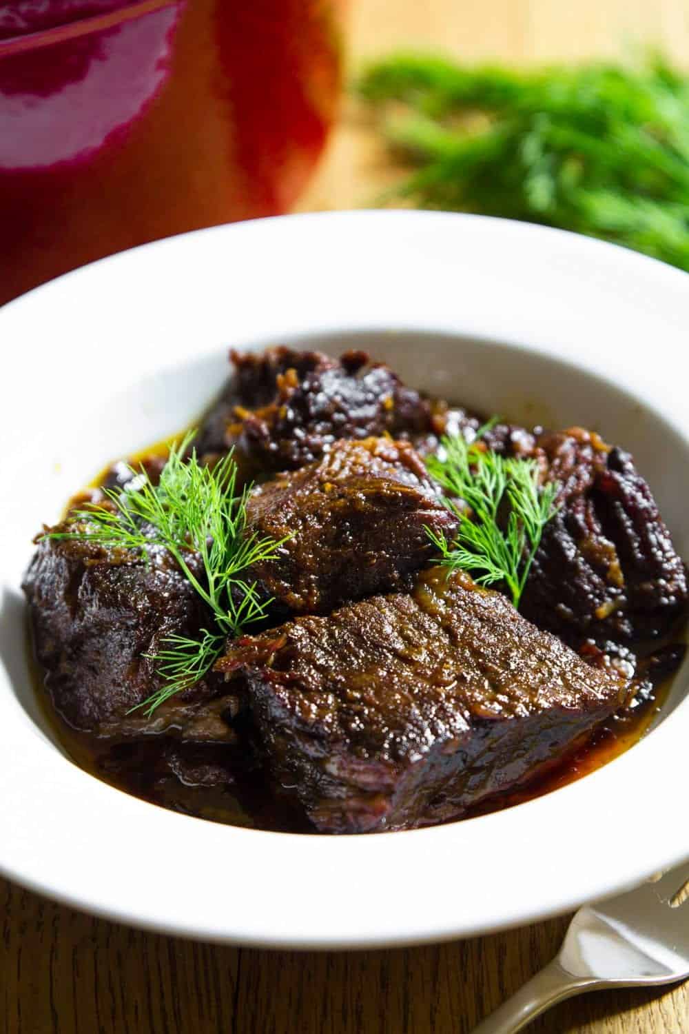 braised beef in a white bowl with fresh dill on top