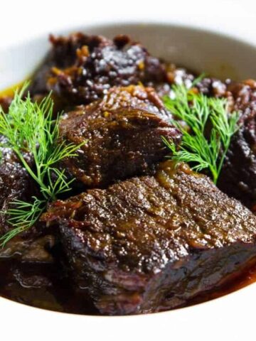 braised beef in a white bowl with fresh dill on top