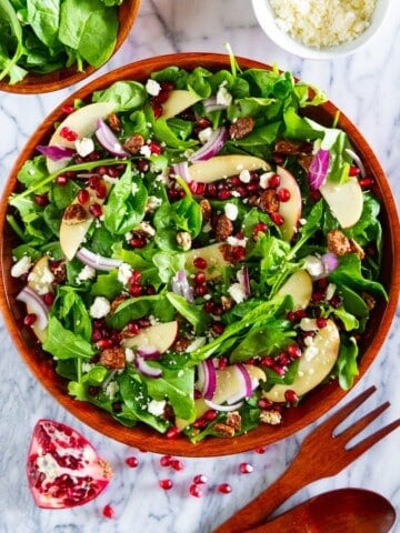 overhead image of spinach pomegranate salad in a wooden bowl