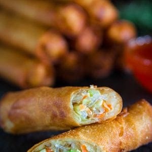 fried spring rolls sliced in half with a glass bowl full of sweet chili sauce next to it.