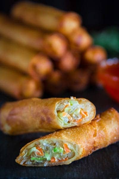 fried spring rolls sliced in half with a glass bowl full of sweet chili sauce next to it.