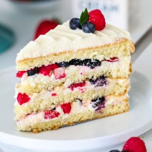 sliced Chantilly cake with berries on top on a white plate with a blue cake stand behind it