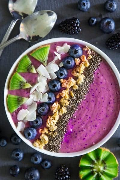blueberry smoothie bowl with chopped kiwi, coconut flakes, granola, and chia seeds on top