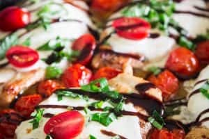cooked chicken breast in a cast iron pan with mozzarella cheese, cherry, tomatoes, basil, and balsamic vinegar on top