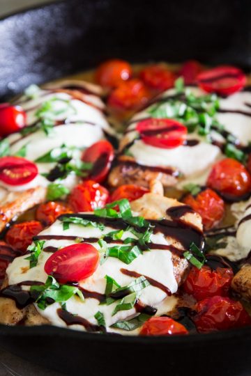 cooked chicken breast in a cast iron pan with mozzarella cheese, cherry, tomatoes, basil, and balsamic vinegar on top