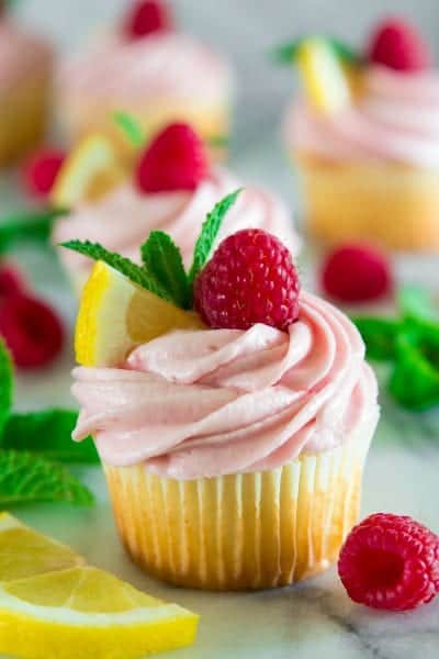 lemon cupcakes with raspberry buttercream topped with raspberries, sliced lemon, and mint