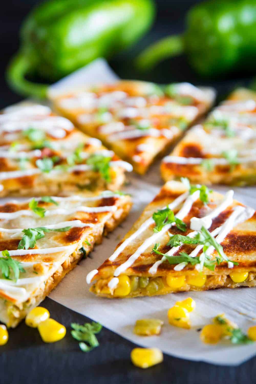 a close up shot of sliced chicken quesadilla with a corn, sour cream, and chopped cilantro on top