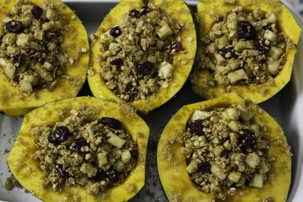 a close up image of halved acorn squashes in a baking dish, stuffed and ready tp be roasted in the oven