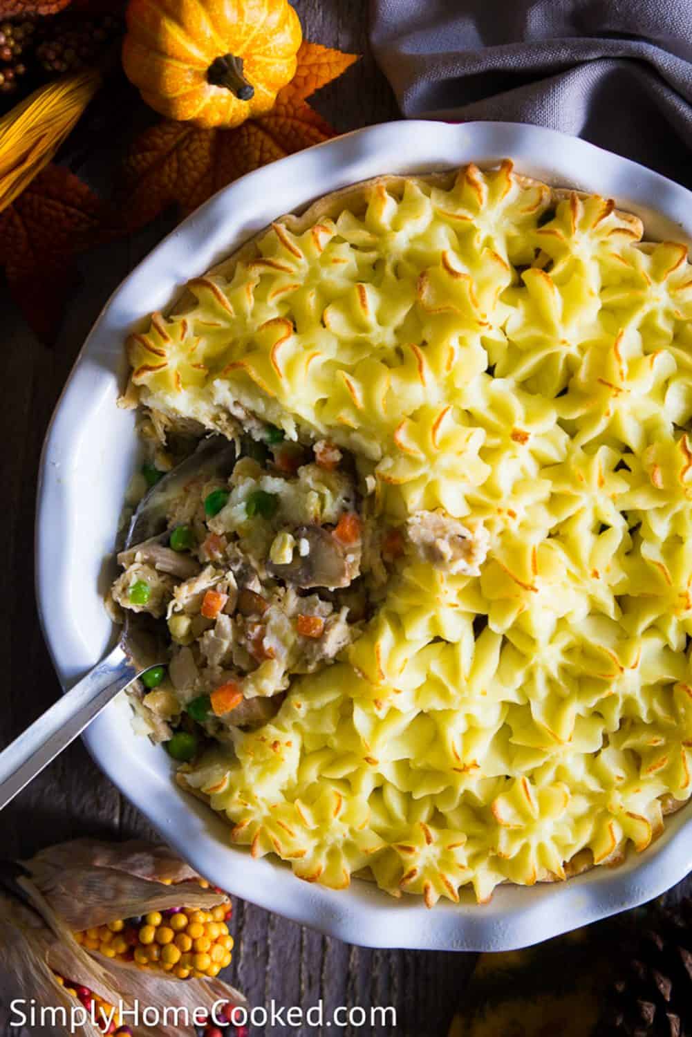 An overhead image of a leftoveer turkey shephers pie with a large spoon in the center and a small pumpkin above it