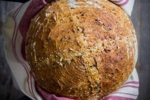 2 hands holding a Harvest Bread loaf using a burgundy and white towel.