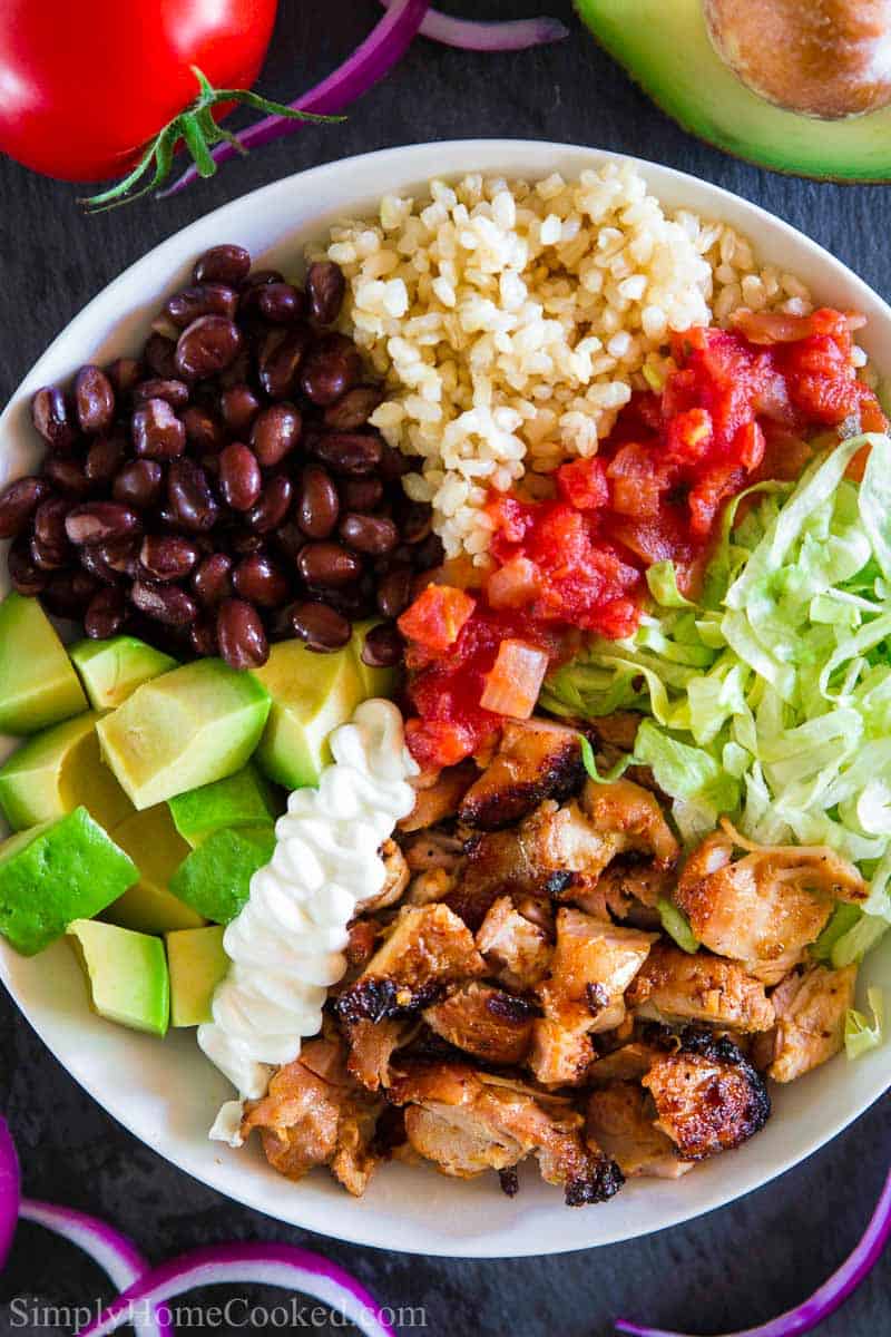 overhead image of chipotle chicken bowl with chicken, avocado, lettuce, salsa, sour cream, black beans, and brown rice