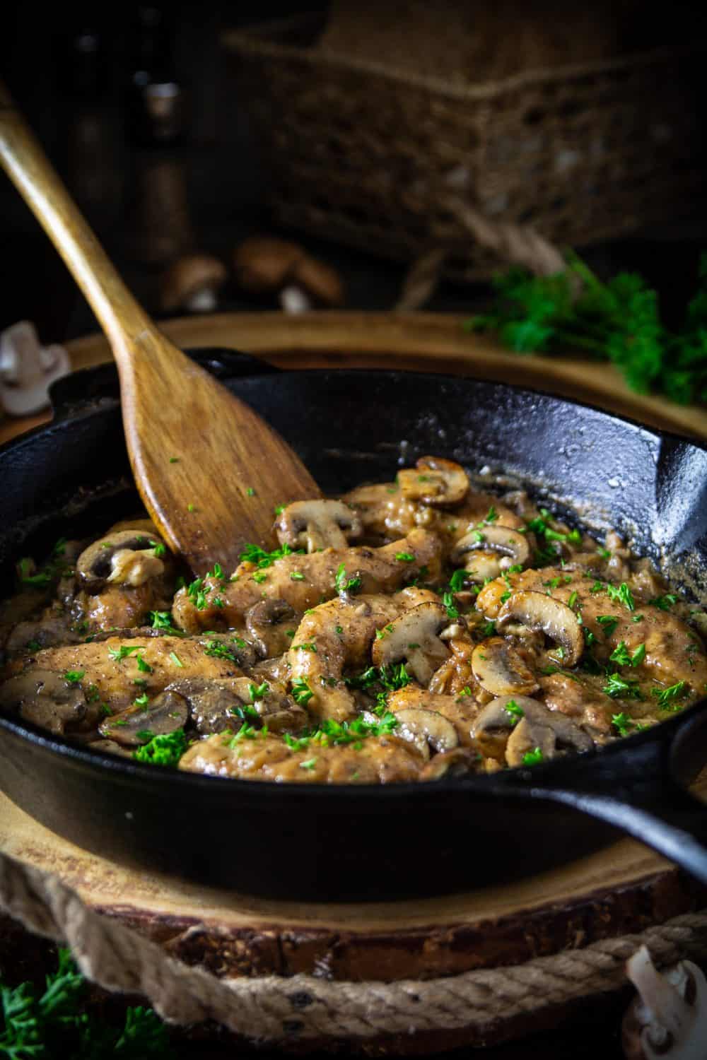 chicken marsala in a cast iron pan with a wooden spoon in the pan