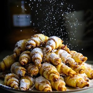 a pile of apricot walnut rugelach with powdered sugar falling on top