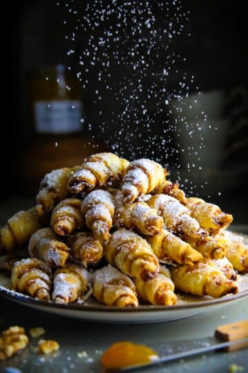 a pile of apricot walnut rugelach with powdered sugar falling on top