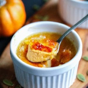 Pumpkin creme brulee with a spoon and pumpkin seeds around the ramekin