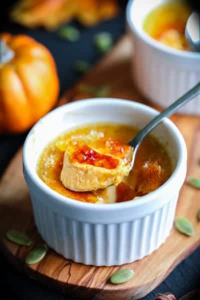 Pumpkin creme brulee with a spoon and pumpkin seeds around the ramekin