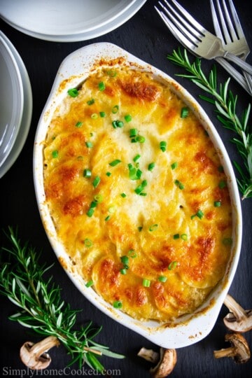baked cheesy scalloped potatoes in a baking with rosemary beside it