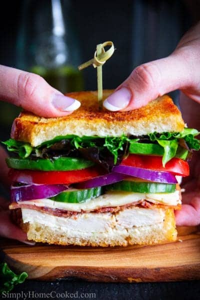 two hands holding a sandwich with lettuce, tomatoes, red onion, bacon, and sour dough bread
