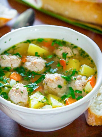 Bowl of Chicken Meatball Soup and crusty bread next to it.