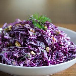 purple cabbage salad in a white plate with walnuts and dill on top