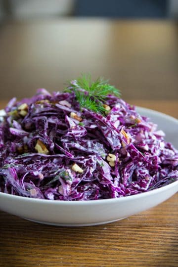 purple cabbage salad in a white plate with walnuts and dill on top